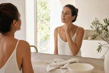 Mujer adulta cuidando suavemente su piel facial en un baño luminoso
