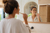 Persona cepillándose los dientes suavemente frente al espejo para cuidar las encías